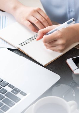 İş konsepti. Kadın dizüstü bilgisayar ve ofis masasında rapor ile proje için not alır. Arka aydınlatma, güneş parlama etkisi, yakın, yan görünüm, kopyalama alanı