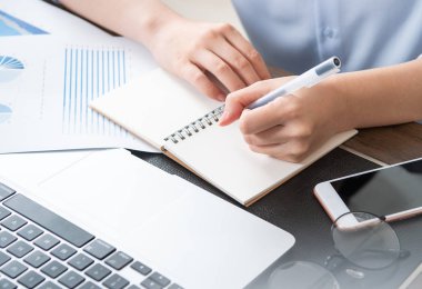 İş konsepti. Kadın dizüstü bilgisayar ve ofis masasında rapor ile proje için not alır. Arka aydınlatma, güneş parlama etkisi, yakın, yan görünüm, kopyalama alanı