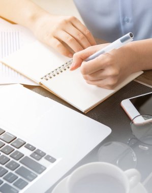 İş konsepti. Kadın dizüstü bilgisayar ve ofis masasında rapor ile proje için not alır. Arka aydınlatma, güneş parlama etkisi, yakın, yan görünüm, kopyalama alanı