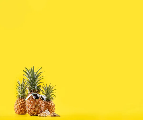 Ananas créatif regardant vers le haut avec des lunettes de soleil et une coquille isolée sur fond jaune, motif de conception d'idée de plage de vacances d'été, espace de copie rapproché — Photo