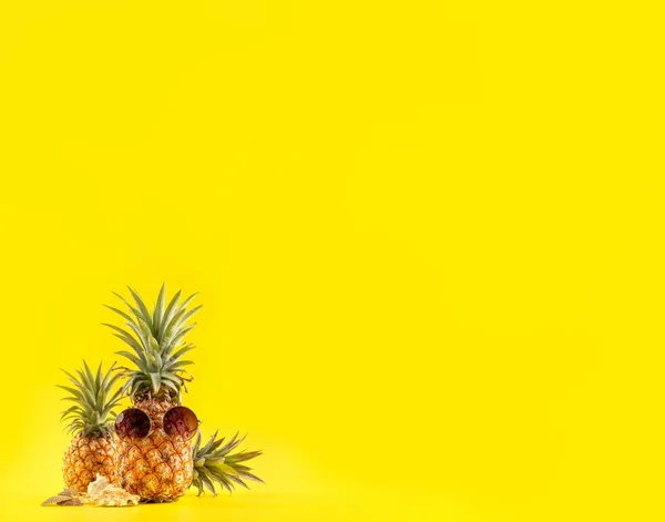 Ananas créatif regardant vers le haut avec des lunettes de soleil et une coquille isolée sur fond jaune, motif de conception d'idée de plage de vacances d'été, espace de copie rapproché — Photo