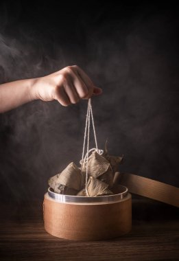 Zongzi, kadın ahşap masada buğulanmış pirinç köftesi yiyecek. Ejderha teknesi festivali Duanwu tasarım konseptinde ünlü lezzetli yemekler. Kapatın, boşluğu kopyalayın.