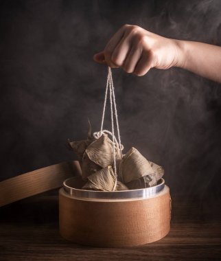 Zongzi, kadın ahşap masada buğulanmış pirinç köftesi yiyecek. Ejderha teknesi festivali Duanwu tasarım konseptinde ünlü lezzetli yemekler. Kapatın, boşluğu kopyalayın.