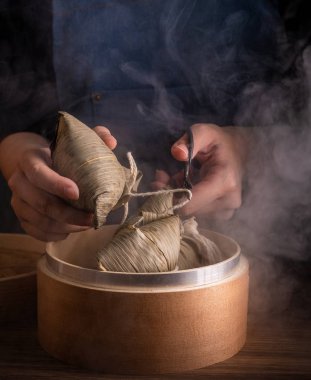 Zongzi, kadın ahşap masada buğulanmış pirinç köftesi yiyecek. Ejderha teknesi festivali Duanwu tasarım konseptinde ünlü lezzetli yemekler. Kapatın, boşluğu kopyalayın.