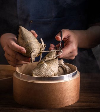 Zongzi, kadın ahşap masada buğulanmış pirinç köftesi yiyecek. Ejderha teknesi festivali Duanwu tasarım konseptinde ünlü lezzetli yemekler. Kapatın, boşluğu kopyalayın.