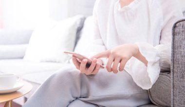 Kanepede oturan ve parlak oturma odasında akıllı telefon kullanarak beyaz Asya genç kadın Yan görünümü, fotokopi alanı, yakın, tasarım konsepti için boş