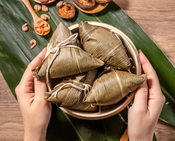 Zongzi, woman eating steamed rice dumplings on wooden table, food in dragon boat festival duanwu concept, close up, copy space, top view, flat lay