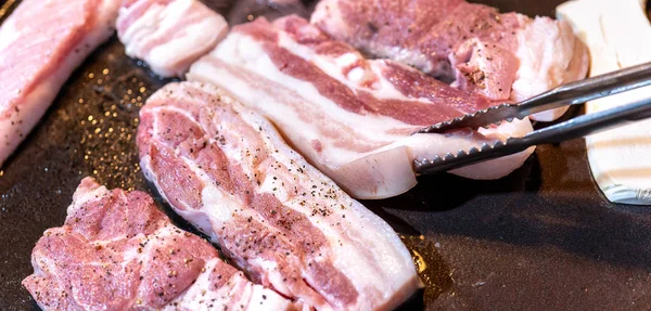 Pan-fried black pork meal in Korea restaurant, fresh delicious korean food cuisine on iron plate with lettuce, close up, copy space, lifestyle