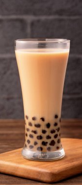 Ahşap masa ve koyu gri tuğla arka planda cam tapyoka inci topu ile lezzetli kabarcık süt çayı, Tayvan popüler yiyecek ve içecek, yakın çekim