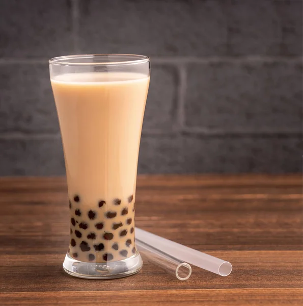 Delicious bubble milk tea with straw in drinking glass on wooden table background, concept of reduce plastic to go in Taiwan, close up, copy space