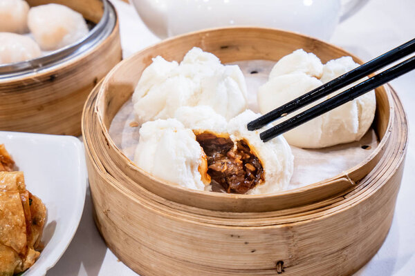 Delicious dim sum, famous cantonese food in asia - Fresh and hot Cha Siu Bao, BBQ pork bun in bamboo steamer in hong kong yumcha restaurant, close up