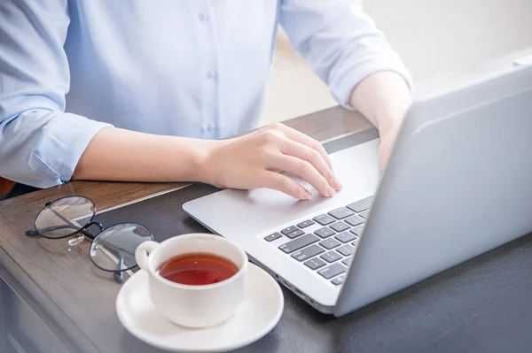 Business concept. Woman in blue shirt typing on computer with coffee on office table, backlighting, sun glare effect, close up, side view, copy space