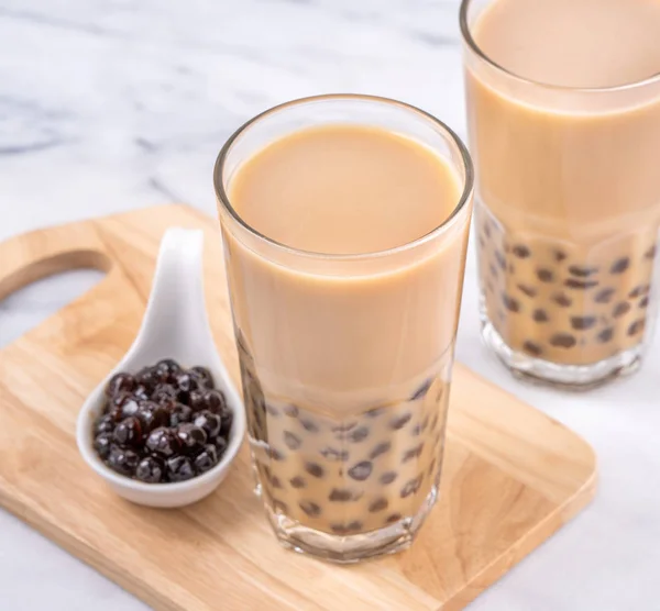 Popular Taiwan drink - Bubble milk tea with tapioca pearl ball in drinking glass on marble white table wooden tray background, close up, copy space