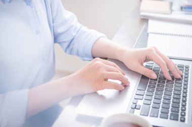 İş konsepti. Ofis masasında kahve ile bilgisayarda yazarak mavi gömlekli kadın, arka aydınlatma, güneş parlama etkisi, yakın, yan görünüm, kopyalama alanı