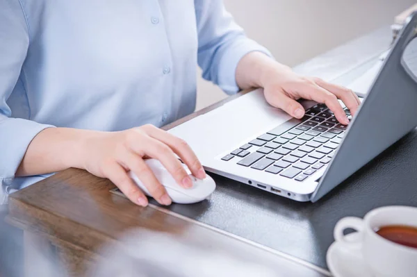 Business concept. Woman in blue shirt typing on computer with coffee on office table, backlighting, sun glare effect, close up, side view, copy space