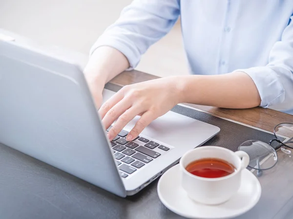 Business concept. Woman in blue shirt typing on computer with coffee on office table, backlighting, sun glare effect, close up, side view, copy space