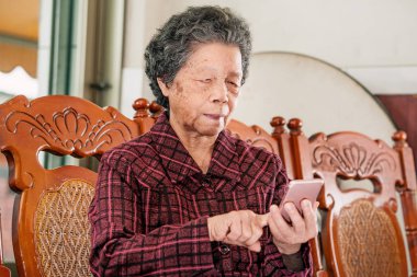 Asyalı yaşlı kadın oturan ve modern akıllı telefon bir şey üzerinden bakarak, evde başkaları ile bağlantı yapma, teknoloji yaşayan, yakın