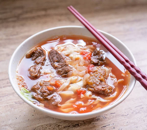 Mie sapi makan ramen dengan saus tomat kaldu dalam mangkuk di atas meja kayu yang cerah, makanan gaya cina terkenal di Taiwan, close up, top view, copy space — Stok Foto