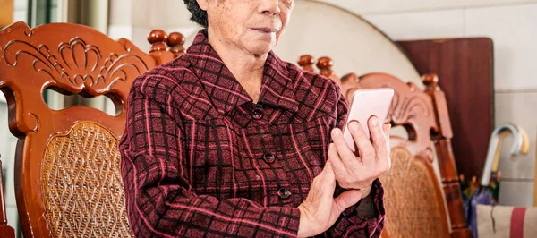 Asian elderly woman sitting and looking through something on modern smartphone, making connection with others at home, living technology, close up — Stock Photo, Image
