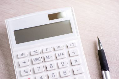 Parlak ahşap masa üzerinde beyaz hesap makinesi ve kalem, analitik ve finansal kar istatistikleri, yatırım riski kavramı, kopya alanı, üst görünüm düz yatıyordu
