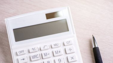 Parlak ahşap masa üzerinde beyaz hesap makinesi ve kalem, analitik ve finansal kar istatistikleri, yatırım riski kavramı, kopya alanı, üst görünüm düz yatıyordu