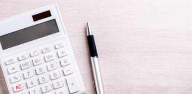 Parlak ahşap masa üzerinde beyaz hesap makinesi ve kalem, analitik ve finansal kar istatistikleri, yatırım riski kavramı, kopya alanı, üst görünüm düz yatıyordu