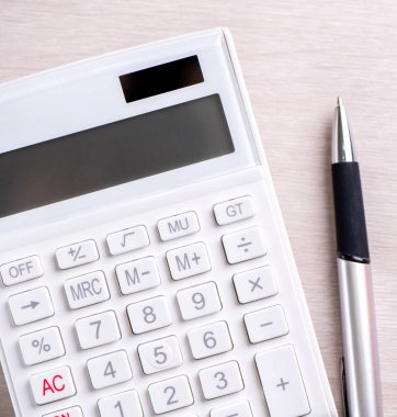 Parlak ahşap masa üzerinde beyaz hesap makinesi ve kalem, analitik ve finansal kar istatistikleri, yatırım riski kavramı, kopya alanı, üst görünüm düz yatıyordu