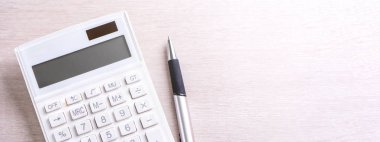 Parlak ahşap masa üzerinde beyaz hesap makinesi ve kalem, analitik ve finansal kar istatistikleri, yatırım riski kavramı, kopya alanı, üst görünüm düz yatıyordu