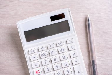 Parlak ahşap masa üzerinde beyaz hesap makinesi ve kalem, analitik ve finansal kar istatistikleri, yatırım riski kavramı, kopya alanı, üst görünüm düz yatıyordu