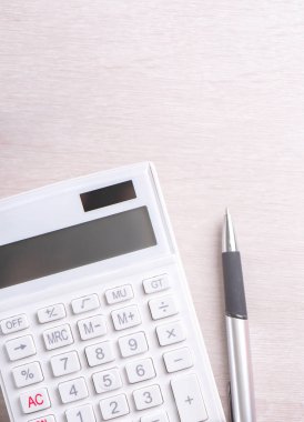 Parlak ahşap masa üzerinde beyaz hesap makinesi ve kalem, analitik ve finansal kar istatistikleri, yatırım riski kavramı, kopya alanı, üst görünüm düz yatıyordu