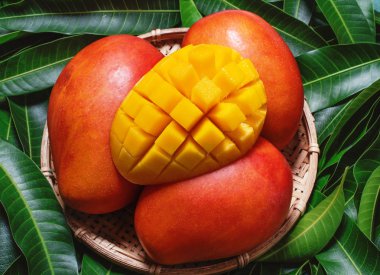Yeşil yaprakları arka plan üzerinde bambu sepeti Taze sulu güzel doğranmış mango meyve, üst görünümü, yakın, makro, kopya alanı. Tropikal yaz konsepti.