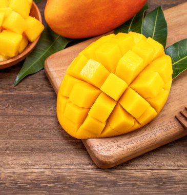 Ahşap kesme tahtası ve rustik ahşap arka plan taze doğranmış mango küpleri. Tropikal yaz meyve konsepti, yakın çekim, makro, kopyalama alanı. 