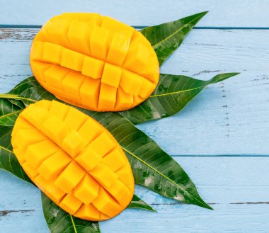 Parlak mavi renkli ahşap arka plan üzerinde yeşil yaprakları ile Taze doğranmış mango. Yukarıda üst görünümü, düz yatıyordu, kopyalama alanı, yakın. Tropikal meyve konsepti.