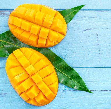 Parlak mavi renkli ahşap arka plan üzerinde yeşil yaprakları ile Taze doğranmış mango. Yukarıda üst görünümü, düz yatıyordu, kopyalama alanı, yakın. Tropikal meyve konsepti.