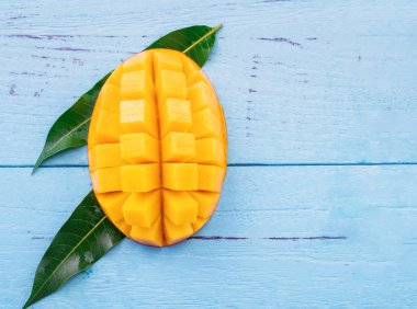 Parlak mavi renkli ahşap arka plan üzerinde yeşil yaprakları ile Taze doğranmış mango. Yukarıda üst görünümü, düz yatıyordu, kopyalama alanı, yakın. Tropikal meyve konsepti.
