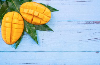 Parlak mavi renkli ahşap arka plan üzerinde yeşil yaprakları ile Taze doğranmış mango. Yukarıda üst görünümü, düz yatıyordu, kopyalama alanı, yakın. Tropikal meyve konsepti.
