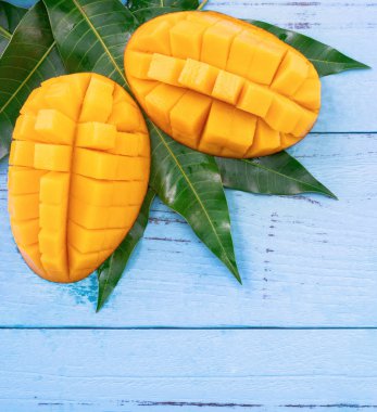 Parlak mavi renkli ahşap arka plan üzerinde yeşil yaprakları ile Taze doğranmış mango. Yukarıda üst görünümü, düz yatıyordu, kopyalama alanı, yakın. Tropikal meyve konsepti.
