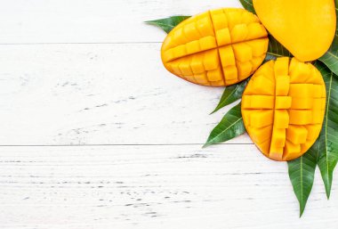 Parlak beyaz renkli ahşap arka plan üzerinde yeşil yaprakları ile güzel doğranmış mango. Yukarıda üst görünümü, düz yatıyordu, kopyalama alanı, yakın. Tropikal meyve konsepti.