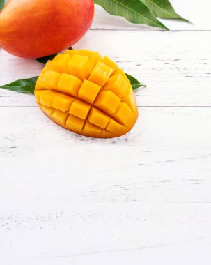 Parlak beyaz renkli ahşap arka plan üzerinde yeşil yaprakları ile güzel doğranmış mango parçaları. Kopya alanı, yakın, makro. Tropikal meyve konsepti.
