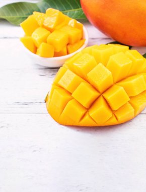 Parlak beyaz renkli ahşap arka plan üzerinde yeşil yaprakları ile güzel doğranmış mango parçaları. Kopya alanı, yakın, makro. Tropikal meyve konsepti.