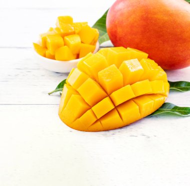 Parlak beyaz renkli ahşap arka plan üzerinde yeşil yaprakları ile güzel doğranmış mango parçaları. Kopya alanı, yakın, makro. Tropikal meyve konsepti.