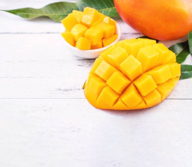 Parlak beyaz renkli ahşap arka plan üzerinde yeşil yaprakları ile güzel doğranmış mango parçaları. Kopya alanı, yakın, makro. Tropikal meyve konsepti.