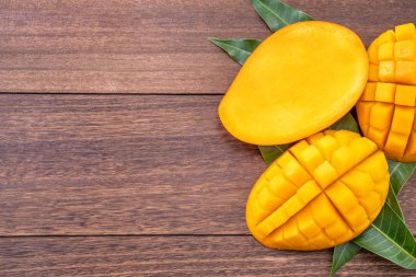 Taze mango - koyu ahşap arka plan üzerinde yeşil yaprakları ile güzel doğranmış meyve. Tropikal meyve tasarım konsepti. Düz yatıyordu. Üst te. Kopyalama alanı.