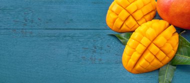 Taze mango-koyu mavi ahşap arka planda yeşil yaprakları ile güzel doğranmış meyve. Tropikal meyve tasarım kavramı. Düz yatıyordu. Üst görünüm. Boşluk Kopyala