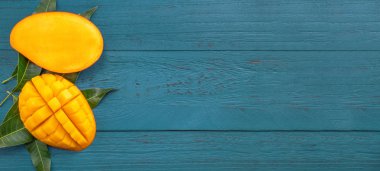 Taze mango-koyu mavi ahşap arka planda yeşil yaprakları ile güzel doğranmış meyve. Tropikal meyve tasarım kavramı. Düz yatıyordu. Üst görünüm. Boşluk Kopyala