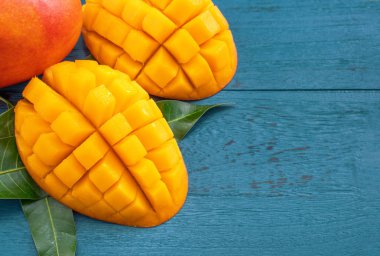 Taze mango-koyu mavi ahşap arka planda yeşil yaprakları ile güzel doğranmış meyve. Tropikal meyve tasarım kavramı. Düz yatıyordu. Üst görünüm. Boşluk Kopyala