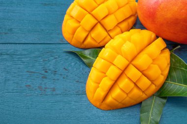 Taze mango-koyu mavi ahşap arka planda yeşil yaprakları ile güzel doğranmış meyve. Tropikal meyve tasarım kavramı. Düz yatıyordu. Üst görünüm. Boşluk Kopyala
