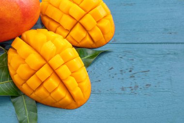 Taze mango-koyu mavi ahşap arka planda yeşil yaprakları ile güzel doğranmış meyve. Tropikal meyve tasarım kavramı. Düz yatıyordu. Üst görünüm. Boşluk Kopyala