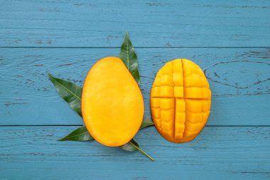 Taze mango-koyu mavi ahşap arka planda yeşil yaprakları ile güzel doğranmış meyve. Tropikal meyve tasarım kavramı. Düz yatıyordu. Üst görünüm. Boşluk Kopyala