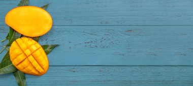 Taze mango-koyu mavi ahşap arka planda yeşil yaprakları ile güzel doğranmış meyve. Tropikal meyve tasarım kavramı. Düz yatıyordu. Üst görünüm. Boşluk Kopyala